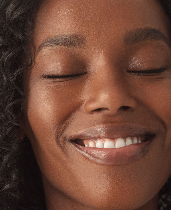 Close-up of a smiling woman with her eyes closed, showing radiant skin and a natural smile.
