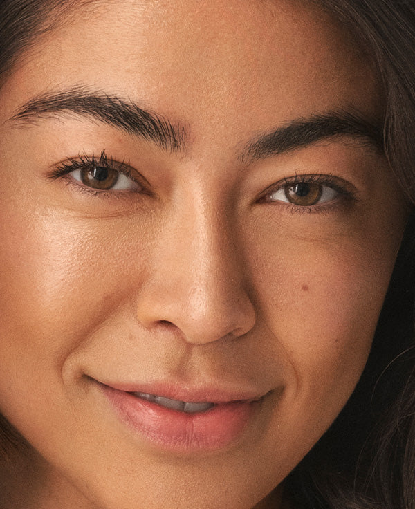 Close-up of a smiling woman looking at the camera, highlighting smooth, natural-looking skin.